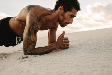 Fit junger Mann trainiert in der Wüste. Männlicher Athlet macht Core-Workout auf einer Sanddüne. Mann macht Plank-Training. - JLPSF20123