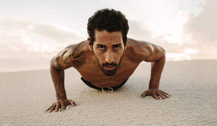 Porträt eines starken jungen Sportlers, der Liegestütze im Wüstensand macht. Ein fitter Mann, der abends in einer Sanddüne trainiert. - JLPSF20125