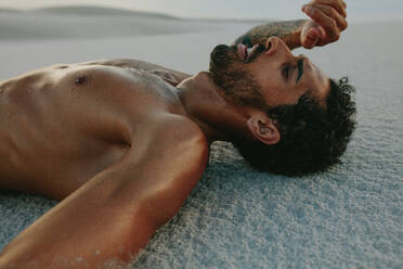 Müder Mann liegt nach intensivem Training auf einer Sanddüne. Sportler ruht sich nach dem Training im Sand aus. - JLPSF20127