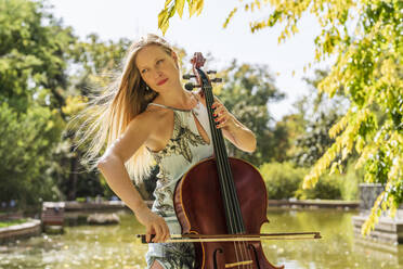 Blonde Frau spielt Cello vor einem See im Park - DLTSF03361