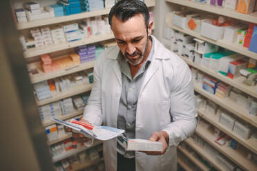 Male pharmacist searching for medicine in pharmacy. Pharmacist holding prescription checking medicine in pharmacy. - JLPSF20160