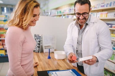 Pharmacist showing and advising medicine to female customer in chemist shop. Pharmacist suggesting medical drug to female buyer in medicine store. - JLPSF20162