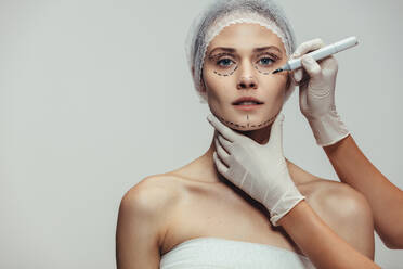 Kosmetikerin zeichnet gepunktete Linien auf das Gesicht einer Frau vor einer plastischen Operation zur Verjüngung des Gesichts. - JLPSF20183