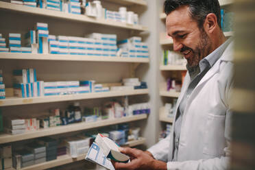 Mature pharmacist with a prescription looking for right medicine in pharmacy. Pharmacist holding prescription and checking medicine in pharmacy. - JLPSF20251