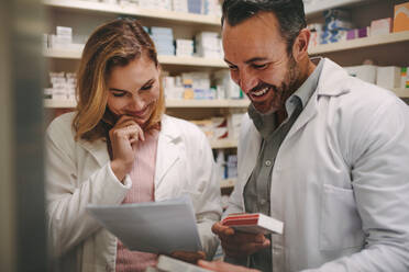 Two dedicated male and female pharmacists looking for the best medicine in the stock while working together in a pharmacy. Pharmacists holding prescription and checking medicine in pharmacy. - JLPSF20254