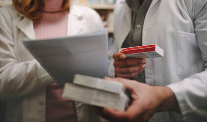 Two chemist with a prescription searching right medicine in pharmacy store. Female pharmacist holding prescription with male checking medicine in pharmacy. - JLPSF20255