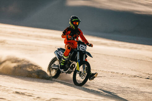 Motocross-Fahrer, der während eines Rennens mit seinem Motorrad fährt. Motorradfahrer, der mit seinem Motorrad auf Wüstensand fährt und eine Spur von Sandstaub hinterlässt. - JLPSF20284