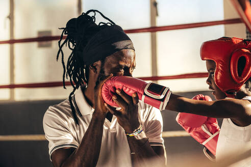 Ein Kind mit Boxhandschuhen und Kopfbedeckung lernt von seinem Trainer Boxen. Ein Trainer bringt einem Kind die Techniken des Boxens bei. - JLPSF20310