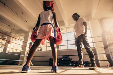 Boxen Kind Training mit seinem Trainer in einem Boxring tragen Boxhandschuhe und Kopfbedeckung. Boxen Trainer Lehre Techniken des Boxens zu einem Kind. - JLPSF20316