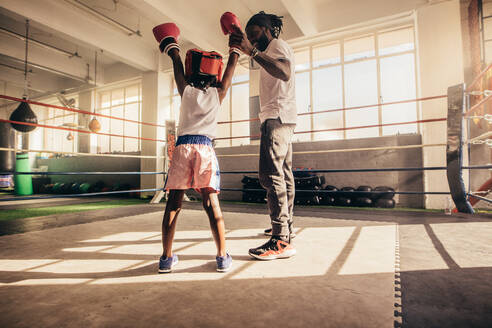 Rückansicht eines Kindes, das mit erhobenen Händen zusammen mit seinem Trainer in einem Boxring steht. Der Trainer hebt die Hand eines boxenden Kindes, das in einem Boxring steht. - JLPSF20317