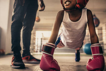 Boxen Kind tut push ups tragen Boxhandschuhe mit seinem Trainer stehen neben ihm. Boxen Kind tun Aufwärmübungen in einem Boxstudio. - JLPSF20318