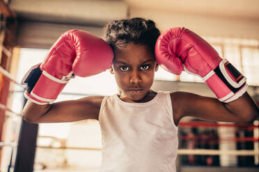 Close up of a kid wearing boxing gloves standing inside a boxing ring. Kid wearing boxing gloves touching her head. - JLPSF20336