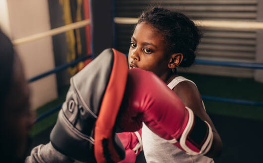 Nahaufnahme eines Kindes, das in einem Boxring trainiert. Ein kleiner Boxer mit Boxhandschuhen übt Schläge auf einem Boxsack. - JLPSF20337