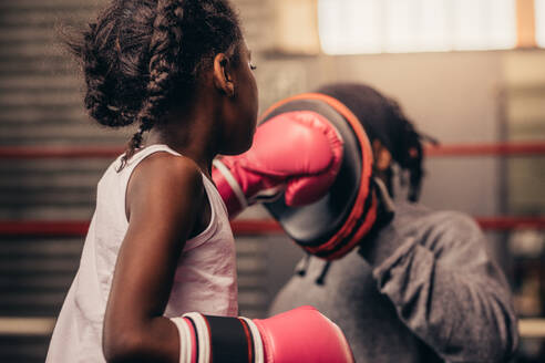 Mädchen mit Boxhandschuhen, das mit ihrem Trainer trainiert. Boxendes Kind, das mit seinem Trainer Schläge auf einem Boxblock übt. - JLPSF20338