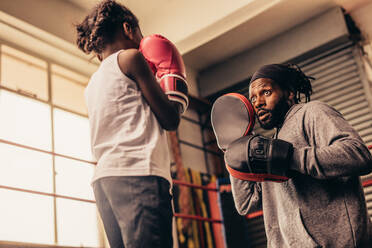 Boxen Kind übt Schläge mit Boxhandschuhen. Boxtrainer mit Boxhandschuhen in den Händen trainiert ein kleines Mädchen. - JLPSF20339