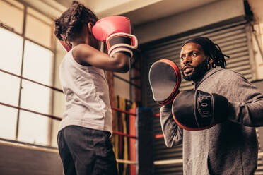 Boxtrainer mit Schlagpolster in den Händen beim Training eines kleinen Mädchens. Boxendes Mädchen beim Training mit ihrem Trainer in einem Boxring. - JLPSF20340