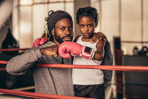 Boxen Kind mit Boxhandschuhen stehen mit ihrem Trainer klopfen ihre Fäuste. Boxen Trainer und Kind schauen zuversichtlich und entschlossen stehen in einem Boxring. - JLPSF20344