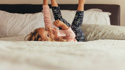 Little girl lying on bed playing with hands and legs raised. Happy little girl playing on bed. - JLPSF20349