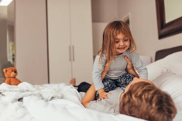 Glücklicher Vater und Tochter spielen zu Hause auf dem Bett liegend. Mann hält ihre Tochter an seiner Brust, während er zu Hause auf dem Bett liegend spielt. - JLPSF20357