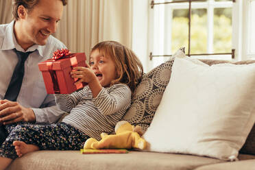 Vater und Tochter sitzen auf einem Sofa und betrachten eine Geschenkbox. Glückliches Mädchen sitzt mit ihrem Vater und hält eine Geschenkbox. - JLPSF20365