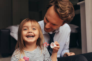 Kleines Mädchen sitzt mit ihrem Vater zusammen und bläst Seifenblasen. Vater und Tochter spielen zusammen und haben Spaß. - JLPSF20369