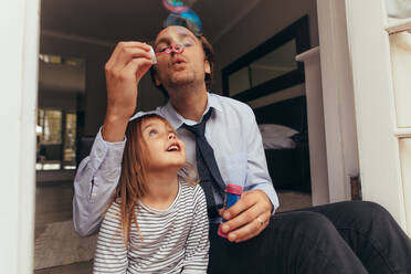 Mann sitzt mit seiner Tochter und bläst Seifenblasen. Vater und Tochter spielen zusammen und haben Spaß beim Blasen von Seifenblasen. - JLPSF20370