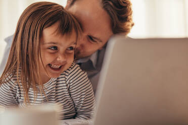 Nahaufnahme eines Mannes, der seine kleine Tochter mit Laptop und Kaffeetasse auf dem Tisch verwöhnt. Der Vater verbringt Zeit mit seiner Tochter, während er zu Hause arbeitet. - JLPSF20377