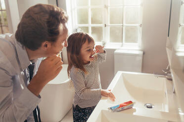 Father and daughter brushing teeth standing in bathroom. Man teaching his daughter how to brush teeth. - JLPSF20381