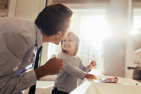 Father and daughter brushing teeth standing in bathroom and looking at each other. Man teaching his daughter how to brush teeth. - JLPSF20382