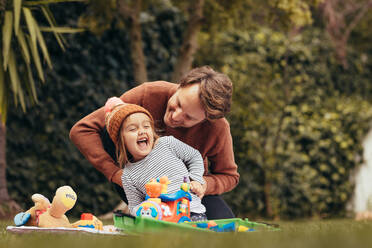 Vater und Tochter sitzen im Park und spielen mit Spielzeug. Vater verwöhnt seine Tochter beim Spielen im Park. - JLPSF20394