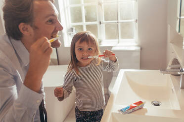 Father and daughter brushing teeth standing in bathroom. Man teaching his daughter how to brush teeth. - JLPSF20402