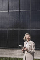 Happy businesswoman standing with tablet PC in front of solar panels - UUF27681
