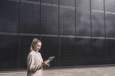 Businesswoman using tablet PC in front of solar panels - UUF27682