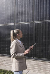 Young businesswoman with tablet PC examining solar panels - UUF27684