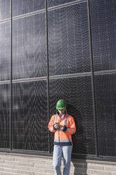 Junge Ingenieurin lehnt sich mit ihrem Mobiltelefon an ein Solarpanel - UUF27698