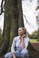 Junge Frau hockt vor einem Baum im Park - UUF27701