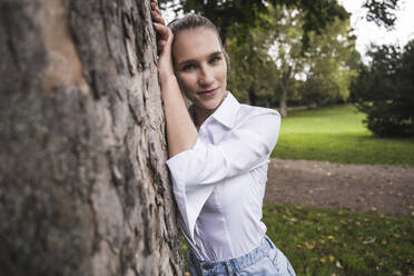 Smiling young woman leaning on tree - UUF27707