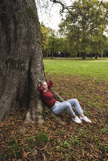 Junge Frau entspannt unter einem Baum im Park - UUF27715