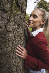 Smiling woman with eyes closed standing by tree - UUF27716