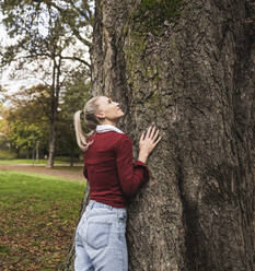 Young woman standing by tree at park - UUF27720