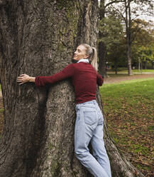 Smiling young woman hugging tree at park - UUF27721