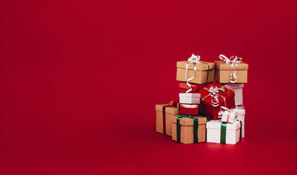 Stapel von Weihnachtsgeschenk-Boxen isoliert auf einem roten Hintergrund. Bunte Geschenk-Boxen mit Bändern und Bögen gebunden. - JLPSF20430