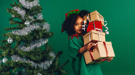 Kleines Mädchen mit einem Stapel von Geschenkboxen neben einem Weihnachtsbaum stehend. Kind hält ihre Weihnachtsgeschenkboxen. - JLPSF20473