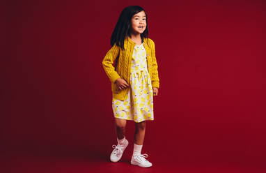 Ganzkörperporträt eines lächelnden asiatischen Kindes vor einem roten Hintergrund. - JLPSF20491