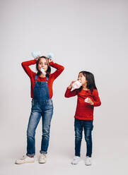 Zwei Kinder essen Zuckerwatte und spielen damit. Mädchen hält sich Zuckerwattekugeln an den Kopf. - JLPSF20497