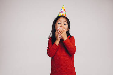 Asiatisches Kind mit Partyhütchen isst Zuckerwatte. Porträt eines kleinen Mädchens, das Zuckerwatte isst. - JLPSF20498