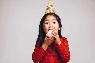 Kleines Mädchen mit einer Partykappe auf dem Kopf isst Zuckerwatte. Nahaufnahme eines Kindes, das Zuckerwatte genießt. - JLPSF20499