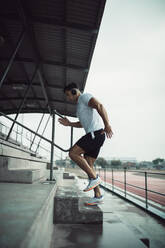 Young muscular man running upstairs on steps at the stadium . Male athlete running on the stadium stand. - JLPSF20509