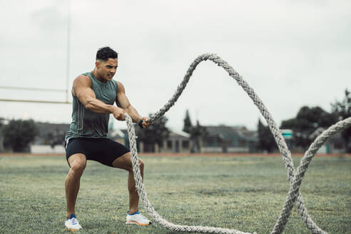 Ein Mann macht ein Fitnesstraining im Freien. Ein fitter junger Mann macht ein Training mit zwei Kampfseilen auf dem Boden. - JLPSF20512