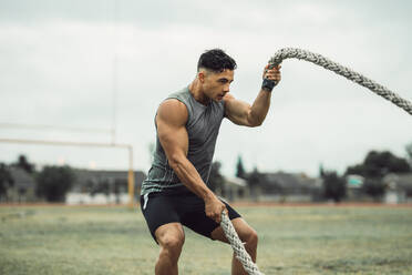 Starker Mann trainiert mit Battle Ropes. Athlet macht Battle Rope Workout im Freien auf einem Feld. - JLPSF20513